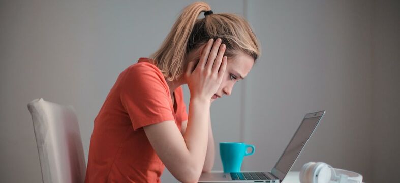 Woman stressed from a divorce holding her head in her hands staring at the computer.