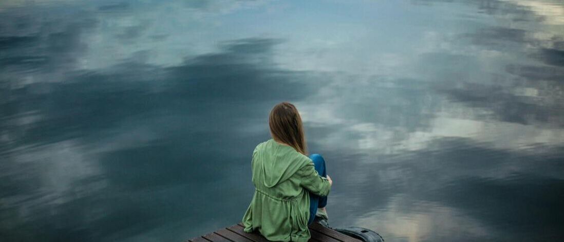 Depressed woman staring off in the distance over a lake.