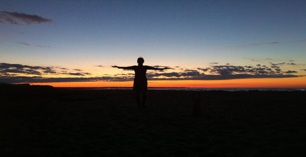 woman at the beach during sunset with their arms out